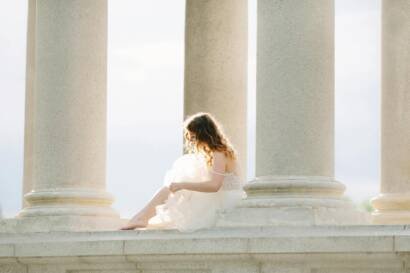 bride in white dress sitting amongst stone columns
