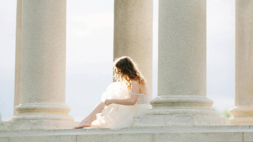 bride in white dress sitting amongst stone columns
