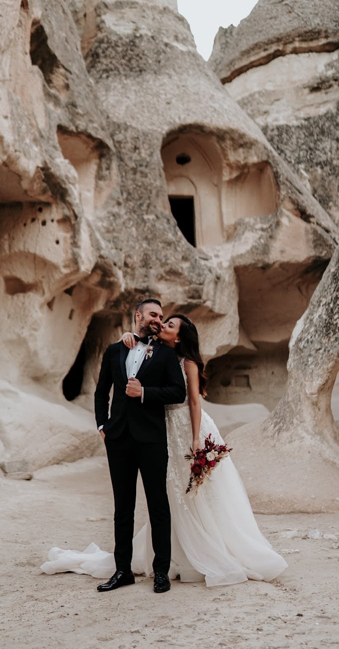 a couple standing on the sand near rock formation