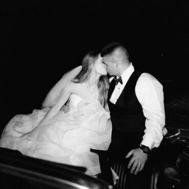 bride and groom kissing while riding on a vintage car