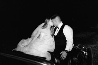 bride and groom kissing while riding on a vintage car