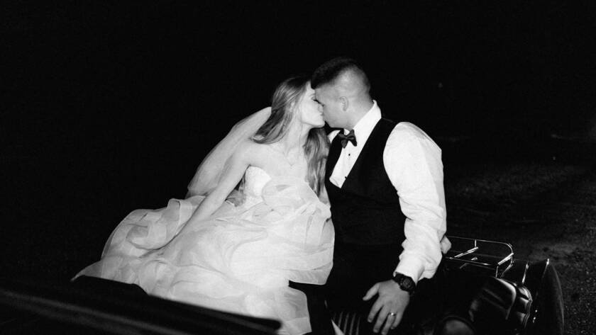 bride and groom kissing while riding on a vintage car