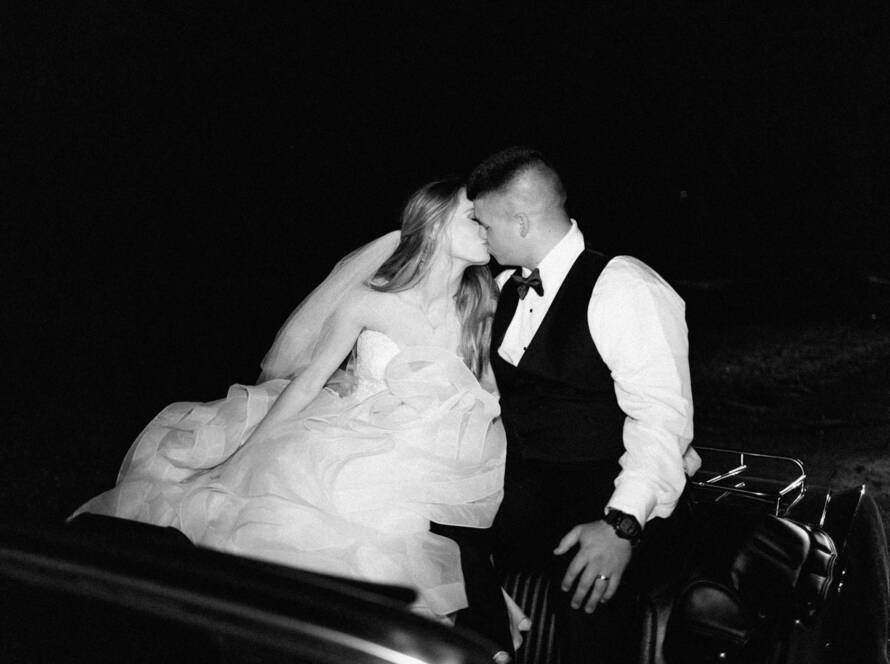 bride and groom kissing while riding on a vintage car